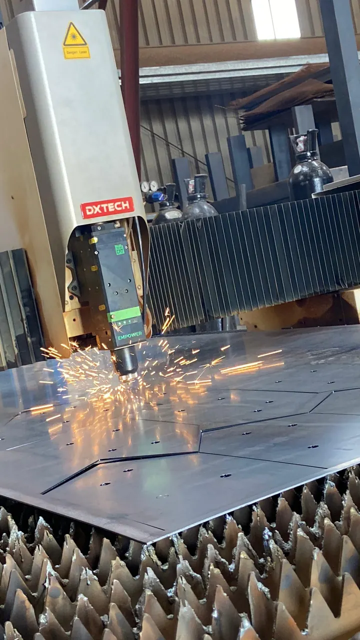 The cutting head of the DXTECH fibre laser close up, sparks off the nozzle and the cut line running out across the sheet.